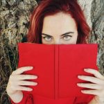Ung rødhåret dame som leser i en rød bok med erotiske noveller
