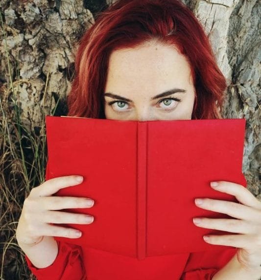 Ung rødhåret dame som leser i en rød bok med erotiske noveller