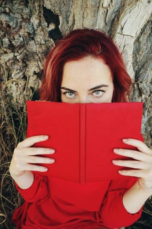 Ung rødhåret dame som leser i en rød bok med erotiske noveller