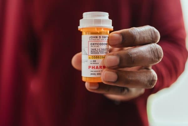 African American man I red shirt at home holding bottle of pain killer oxycodone