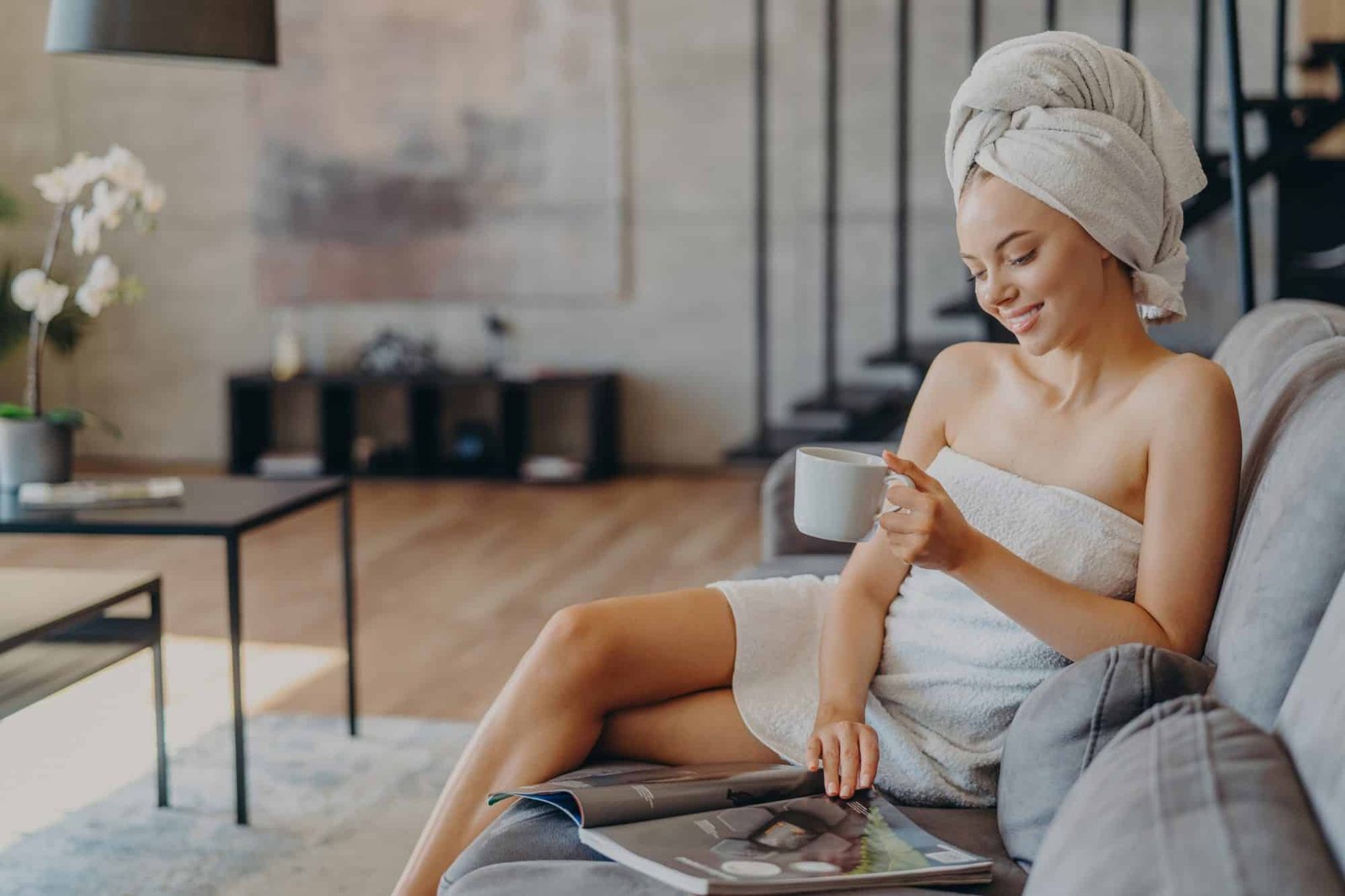 relaxed satisfied woman has healthy skin reads magazine poses with cup