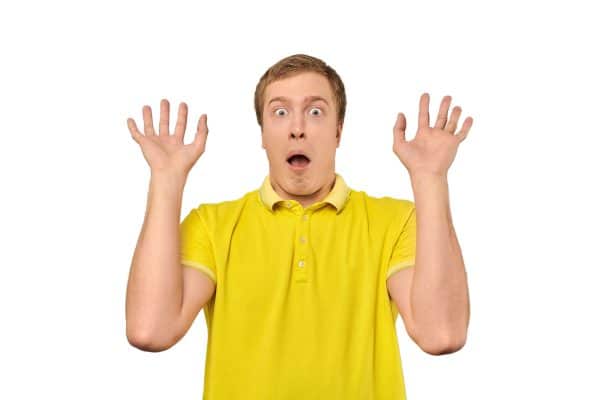Scared young man with hands up in yellow Polo T-shirt, white isolated background