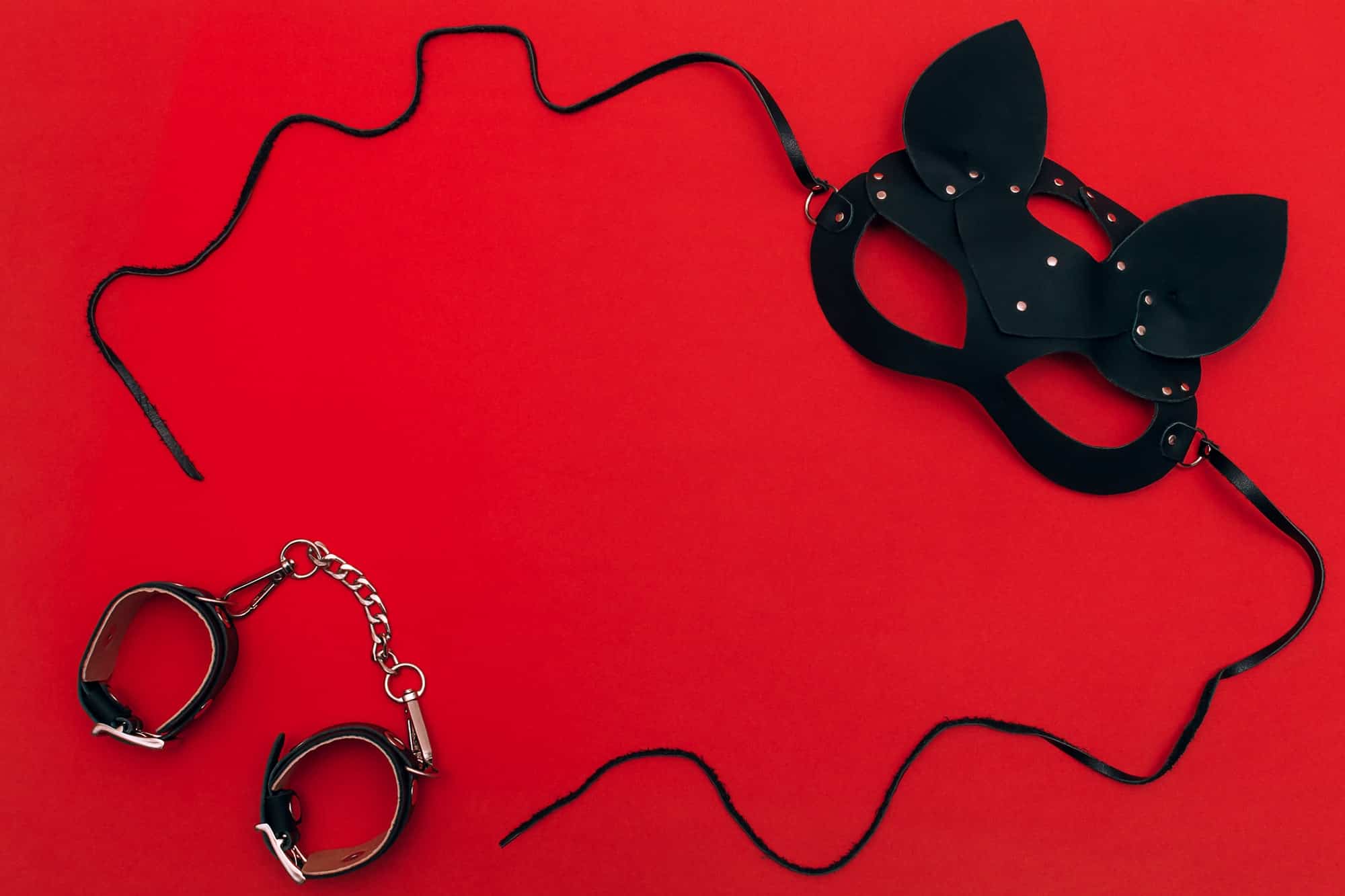 Black leather cat mask on a red background.Concept of Valentine's Day, BDSM communities