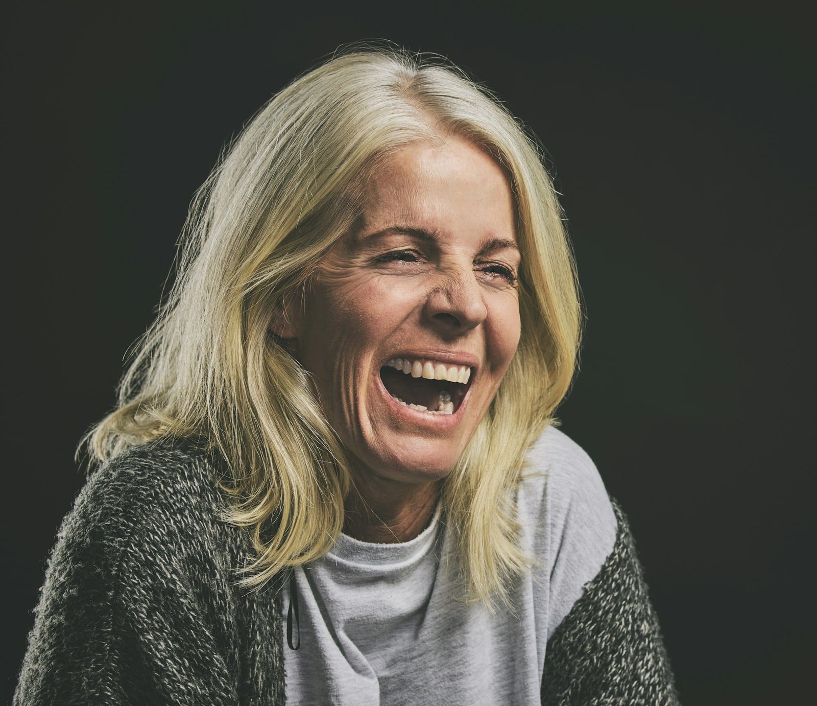 Mental health, depression and woman with bipolar laughing in dark studio. Girl with schizophrenia,