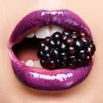 Beguiling blackberry. Shot of a woman wearing purple lipstick and biting into a blackberry.