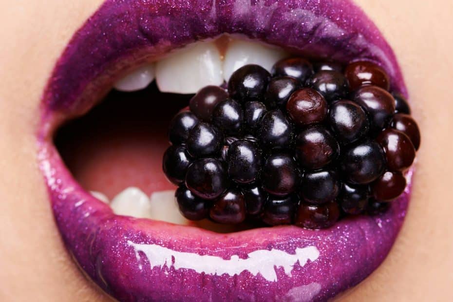 Beguiling blackberry. Shot of a woman wearing purple lipstick and biting into a blackberry.