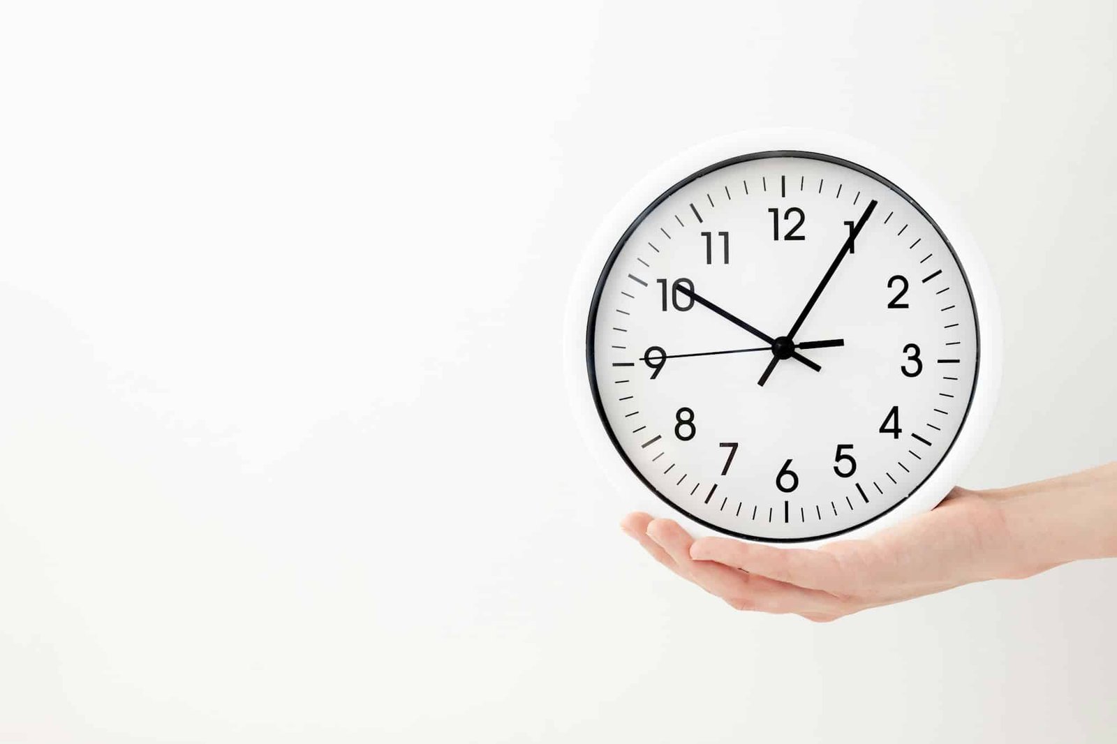 clock, white clock hands on a white background, a female hand holds a round clock with black arrows