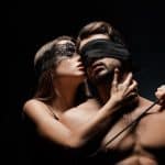 BDSM dame står bak og kjærtegner mann med blindfold