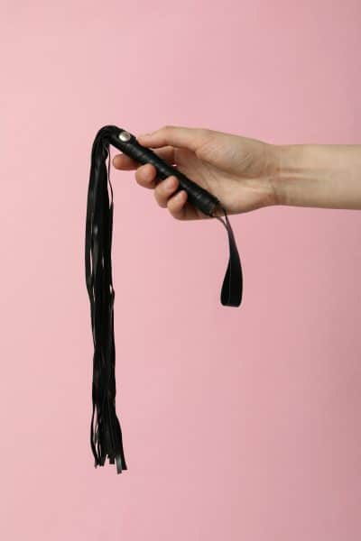 Flogger in hands on a pink background.