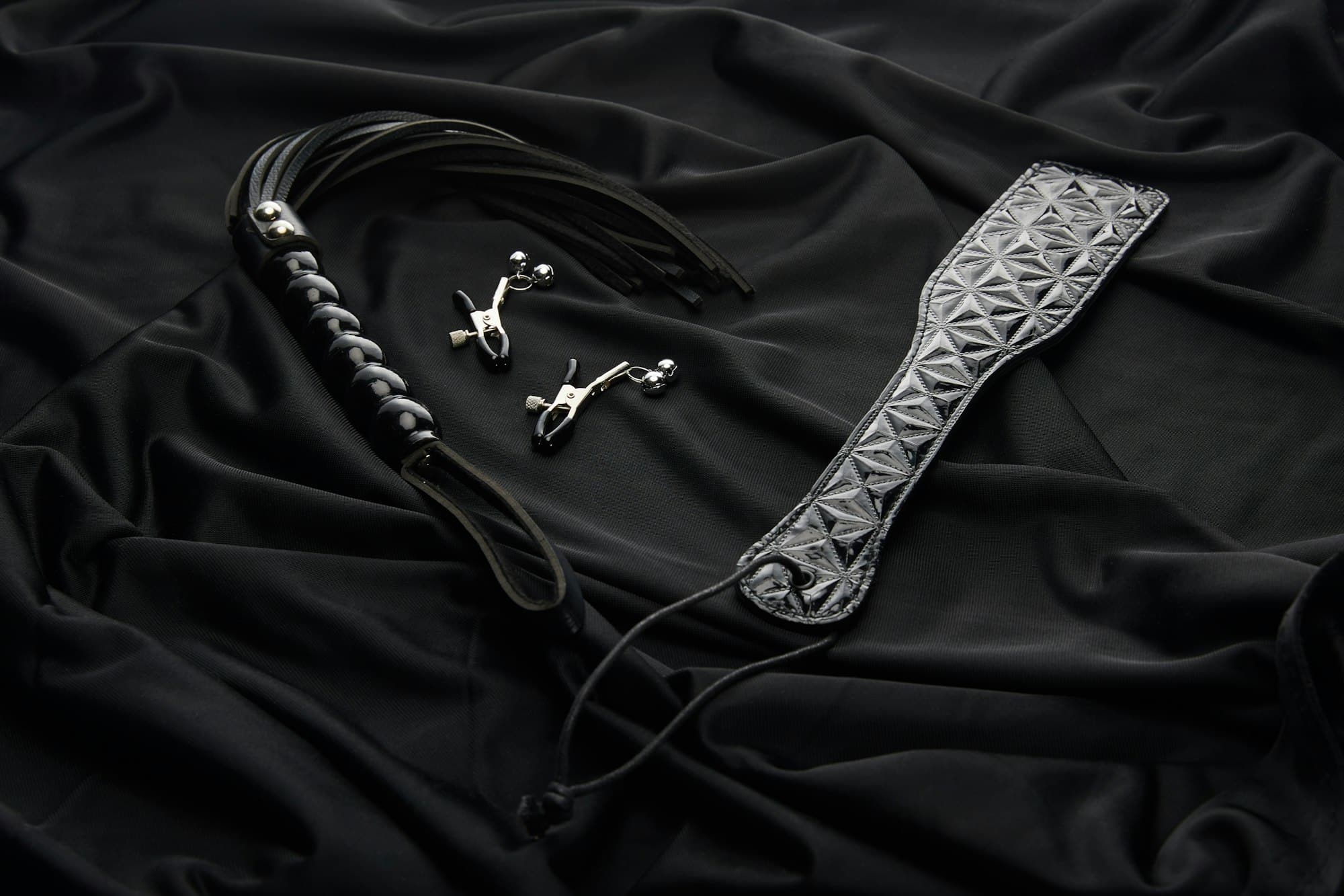 leather and metal sex toys on black textile background