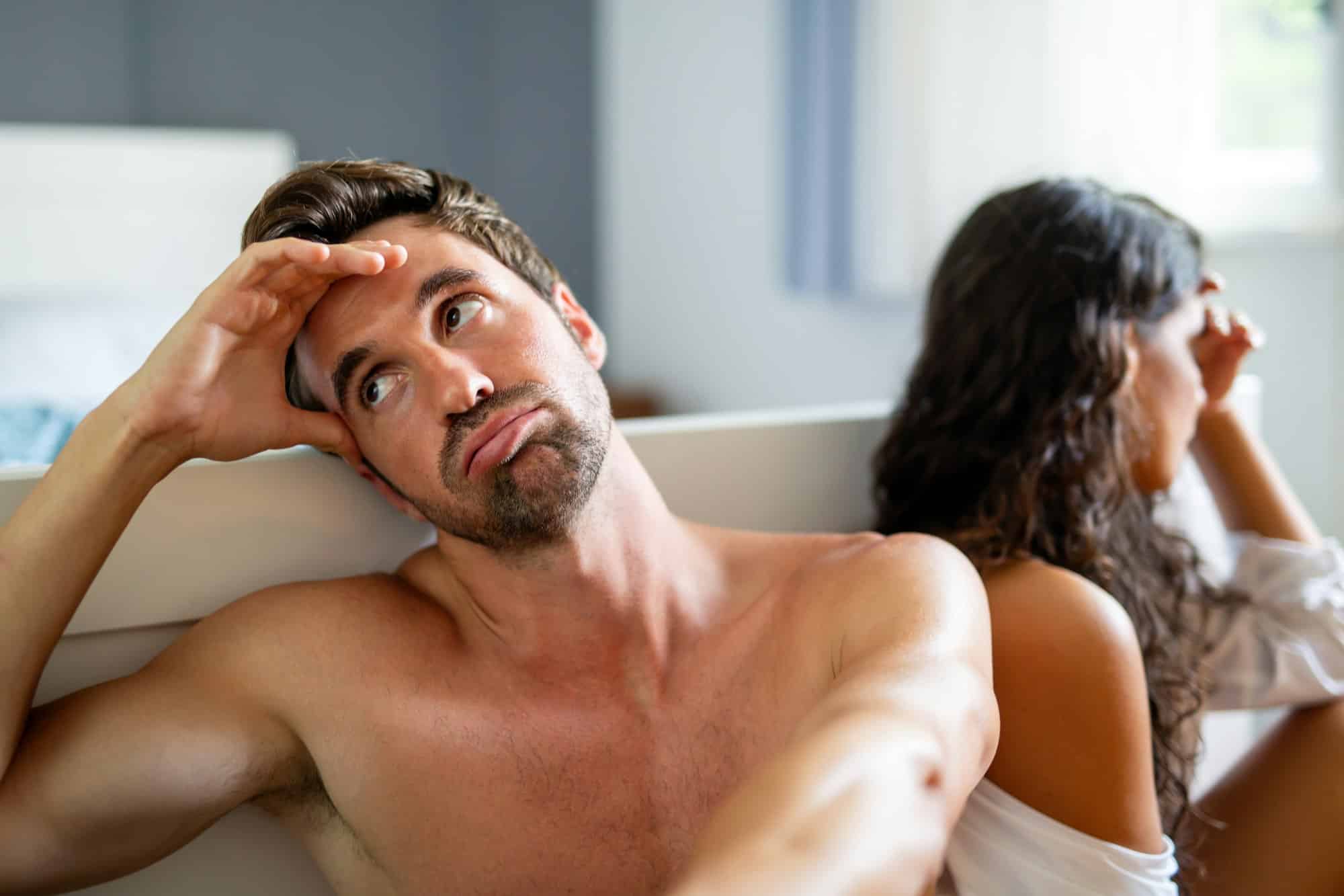 Håndtere uventede sexopplevelser: Naken mann og dame sitter ved sengen og kommuniserer dårlig