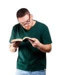 Young bearded Caucasian man in glasses reading a book with a great interest
