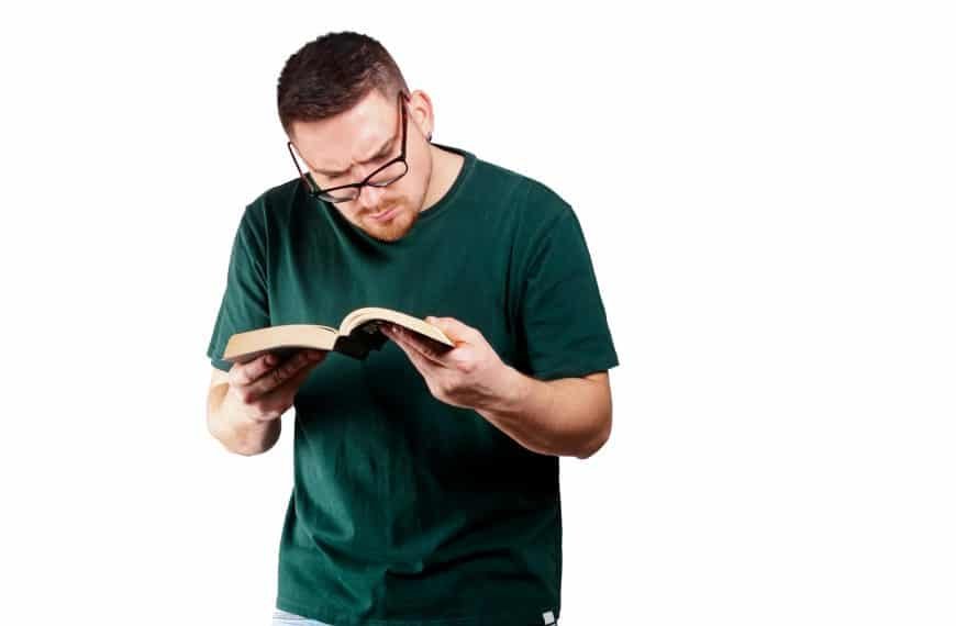 Young bearded Caucasian man in glasses reading a book with a great interest