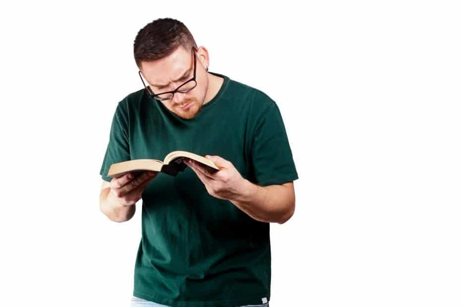 Young bearded Caucasian man in glasses reading a book with a great interest