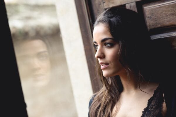 Sexy vakker dame står ved et vindu og spionerer på sine naboer