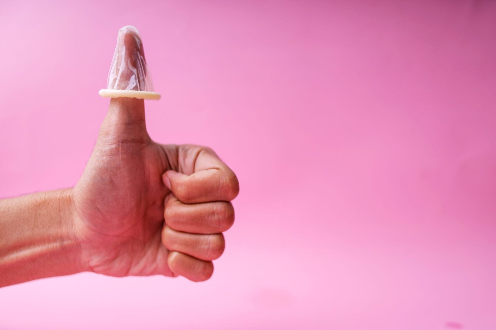 Rosa bakgrunn, mannlig hånd som gir "thumbs up" med en kondom tredd ned over tommelen. Illustrasjon til artikkel om seksuelt samtykke.