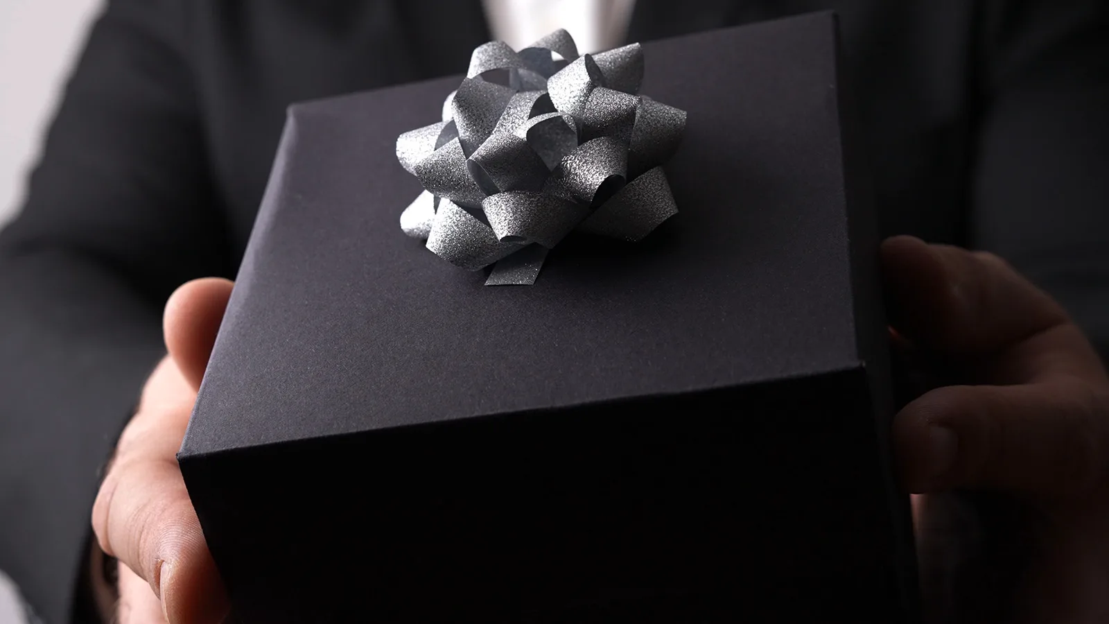 Mann med dress holder en sort gave formet som en boks med sølv sløyfe