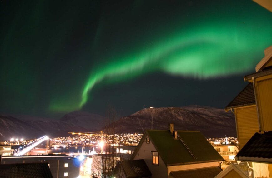 Bilde over swinger byen Tromsø på natt, med nordlys over byen