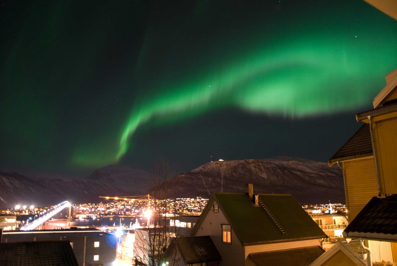 Bilde over swinger byen Tromsø på natt, med nordlys over byen