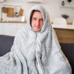 En mann sitter på sofaen med et teppe rundt seg. Aftercare.