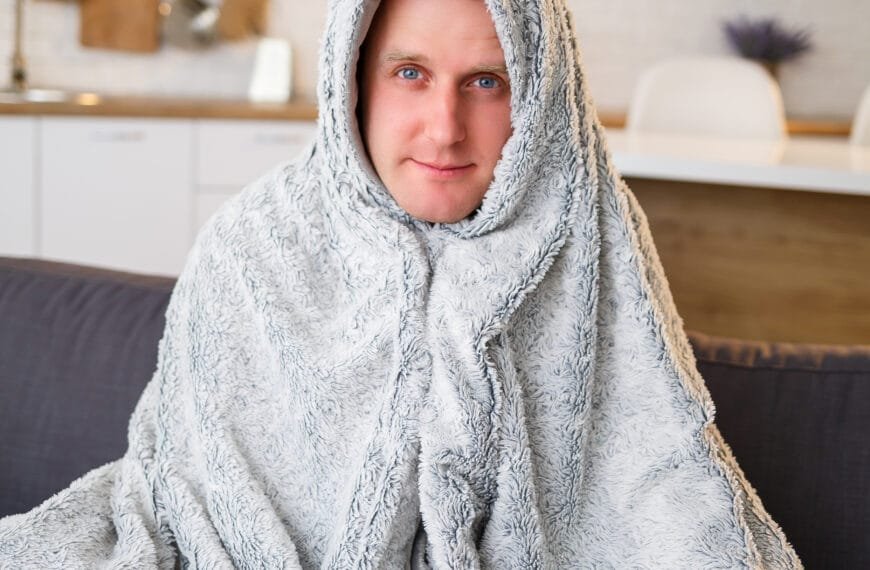 En mann sitter på sofaen med et teppe rundt seg. Aftercare.