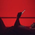 Dame ligger på ryggen og sender tekstmelding. Rød sexy bakgrunn