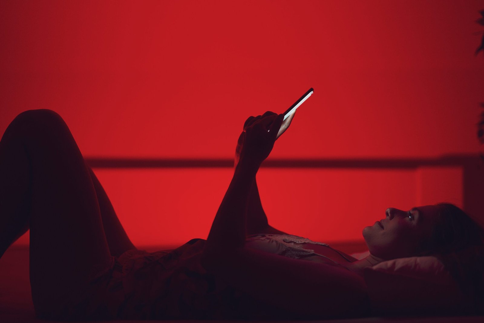 Dame ligger på ryggen og sender tekstmelding. Rød sexy bakgrunn