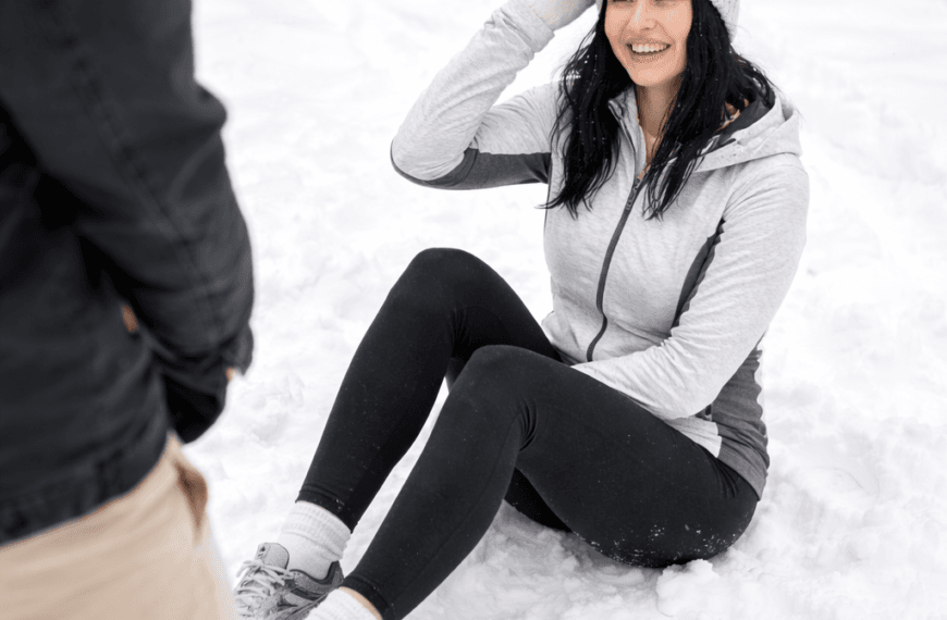 Vakker dame iført treningstøy sitter i snøen etter å ha falt