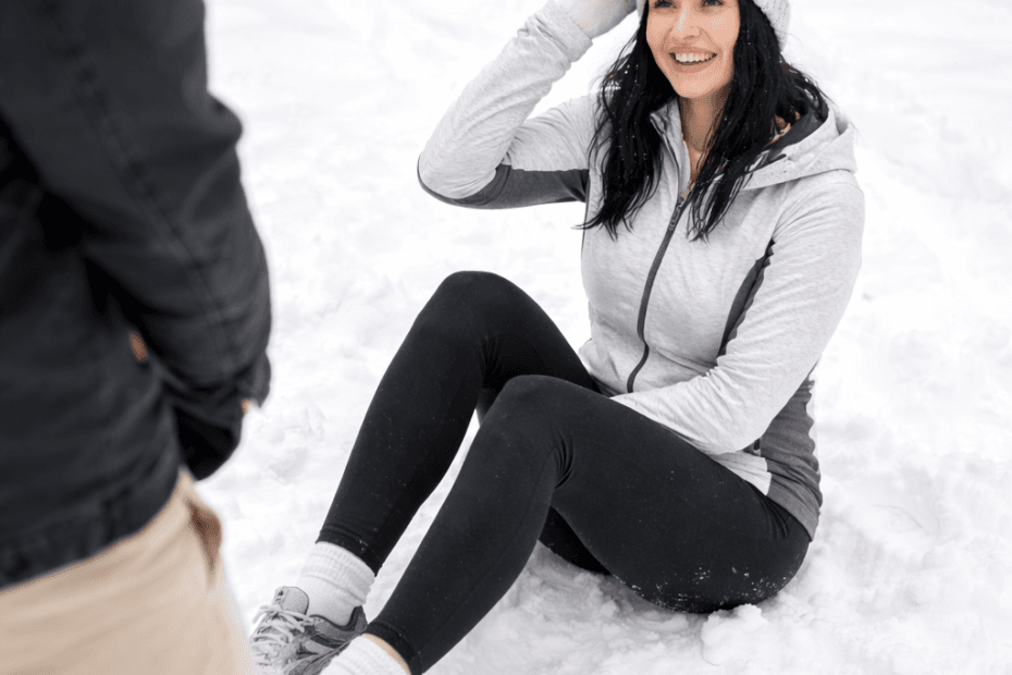 Vakker dame iført treningstøy sitter i snøen etter å ha falt
