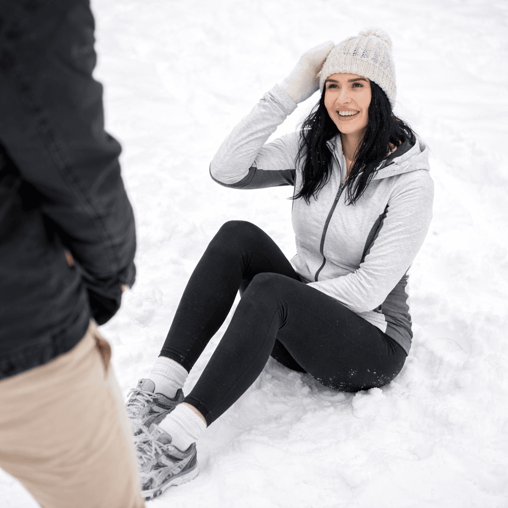 Vakker dame iført treningstøy sitter i snøen etter å ha falt
