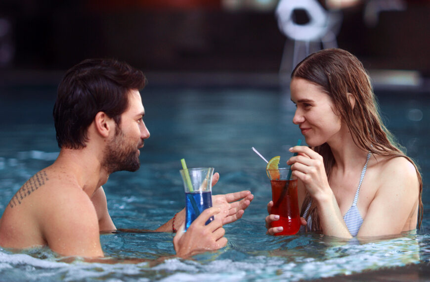 Pen dame og mann i en jacuzzi drikker fargerike drinker